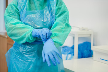 Dedicated medical professional in sterile gown and blue apron meticulously prepares, putting on...