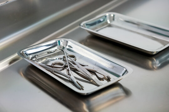 Clean sterile surgical instruments precisely arranged in a shining metal tray on a reflective counter, representing essential hospital and medical procedures