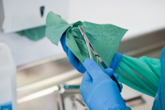 A healthcare professional's gloved hands meticulously clean and sterilize a surgical instrument with a green sterile cloth, ensuring optimal hygiene and safety protocols