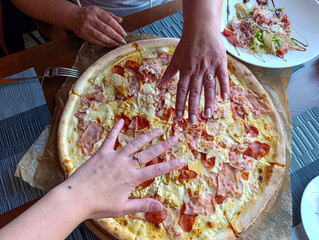 A person reaching for a pizza on a table with plates of food