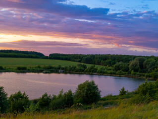 A view of a lake in the middle of a grassy field at sunset