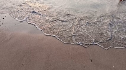 Gentle waves softly wash over the sandy beach at sunset