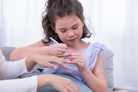 Kids, mother, bonding, beauty, nailcare, young biracial girl carefully paints Asian mother’s nails at home, reversing roles in a sweet parenting moment filled with learning, love, and fun connection