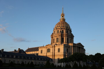 Obraz premium The grand golden dome of Les Invalides in Paris gleams under the warm light of golden hour. This iconic French landmark showcases magnificent classical architecture against a clear blue sky. 