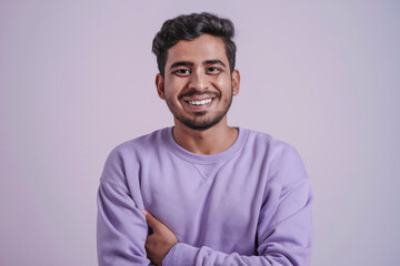 Fototapeta premium Cheerful young man in light purple sweatshirt smiling confidently with folded arms standing against pastel studio background