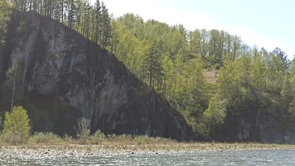 A breathtaking view of a rocky cliffside adorned with lush green trees, alongside a peaceful river. This picturesque landscape showcases the beauty of nature, perfect for tourism.