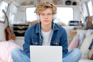 Caucasian teen male with headphones using laptop in cozy room