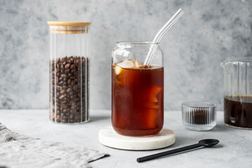 Cold brew coffee in a glass with ice on a marble stand on a light background with coffee beans