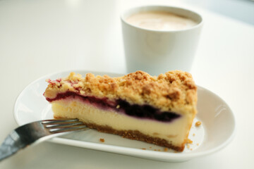 Berry crumble cheesecake with a fork, paired with a creamy cappuccino in a soft natural light. Close view.