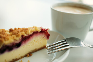 Berry crumble cheesecake with a fork, paired with a creamy cappuccino in a soft natural light. Close view.