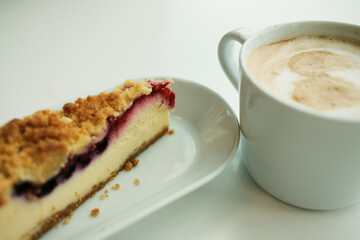Close-up view of creamy berry crumble cheesecake paired with a frothy cappuccino in a white ceramic mug.