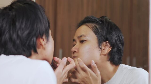 Close-up of an Asian woman applying acne spot treatment in front of a mirror. Focus on skincare routine, blemish care, and self care for healing pimples and maintaining clean, healthy facial skin.
