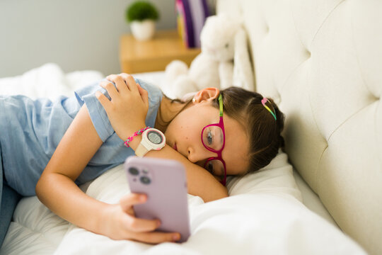 Bored young girl lying in bed using smartphone