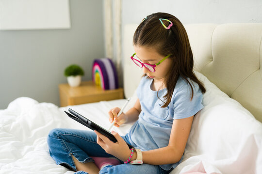 Latin girl using digital tablet and stylus on bed - Powered by Adobe