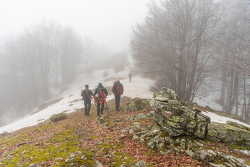 Gruppo di escursionisti visti di spalle seguono il sentiero Italia parzialmente coperto di neve