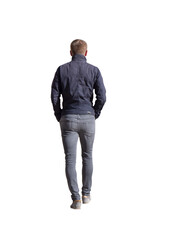Homme  jeune vu de dos dans la trentaine, marchant calmement en extérieur par temps automnal, portant une veste bleu marine, un jean gris ajusté et des chaussures claires, style urbain décontracté