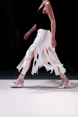 Cropped female figure dressed in a chic fancy crop top and creative white skirt walking on black...
