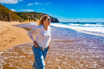 Portrait of beautiful mid adult woman enjoying walk on sandy beach in summertime. Side view. Amado...