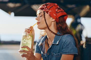 Lifestyle woman wearing modern boho-western denim street style drinks refreshing lemonade outdoors...