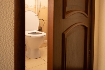 A clean bathroom features a white toilet seen through an open wooden door. The floor is tiled, and...