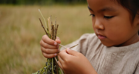 Young girl carefully crafting a bundle of twigs and grass in a serene outdoor setting, showcasing creativity and connection with nature through hands-on activity