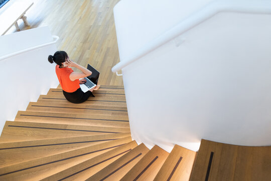 Woman sitting on staircase using smart phone and laptop