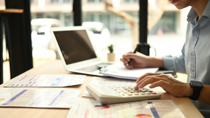 Close-up view of a Business analyst, a man using a calculator to evaluate financial charts and...