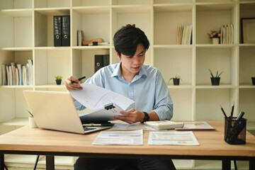 Young professional businessman reviewing financial charts and data with a laptop and calculator on...