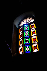 Vertical stained glass window features vibrant geometric pattern with red, green, yellow, white,...