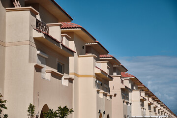 Perspective view of identical beige townhouses under bright blue sky. Row of modern townhouses with Mediterranean design. 
