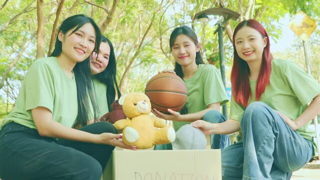 Group of young women happily volunteer together holding donation boxes at a public park in good spirits.