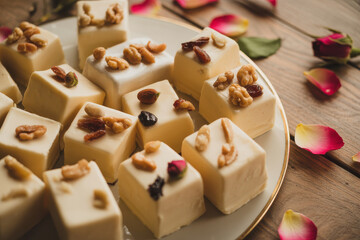 Close up of white cubed confectioneries topped with nuts on a plate with rose petals on wood