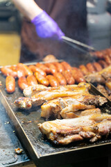 Juicy slices of grilled wild boar meat being roasted over open flames at a night market food stall. The smoky aroma and charred edges highlight the rustic and flavorful appeal of traditional street cu