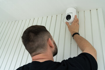 A professional technician installs a rotating surveillance camera on a house wall. Installation and...