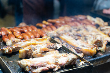 Juicy slices of grilled wild boar meat being roasted over open flames at a night market food stall. The smoky aroma and charred edges highlight the rustic and flavorful appeal of traditional street cu
