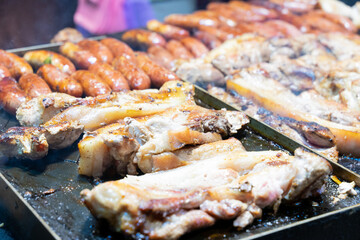 Juicy slices of grilled wild boar meat being roasted over open flames at a night market food stall. The smoky aroma and charred edges highlight the rustic and flavorful appeal of traditional street cu