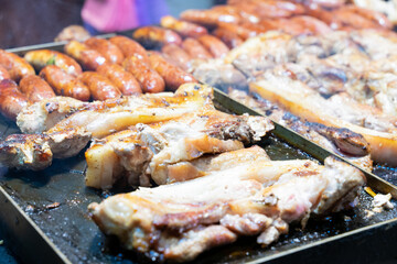 Juicy slices of grilled wild boar meat being roasted over open flames at a night market food stall. The smoky aroma and charred edges highlight the rustic and flavorful appeal of traditional street cu