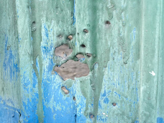 A close-up of the entrance hole from a shotgun blast distressed metal siding with peeling blue and...