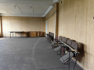 An abandoned theater interior showing rows of old, folded seats and wooden wall paneling.
