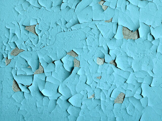 Close-up of peeling blue paint revealing a weathered, textured wall.