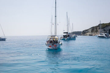 abstract blur sailboats on clear blue Ionian Sea with rocky coastline in distance