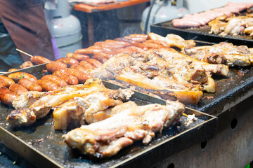 Juicy slices of grilled wild boar meat being roasted over open flames at a night market food stall....