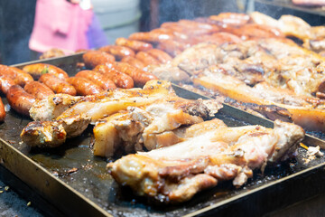 Juicy slices of grilled wild boar meat being roasted over open flames at a night market food stall....