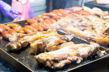 Juicy slices of grilled wild boar meat being roasted over open flames at a night market food stall. The smoky aroma and charred edges highlight the rustic and flavorful appeal of traditional street cu