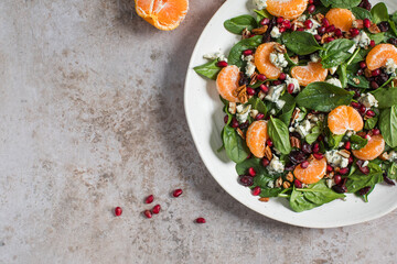 An appetizing festive salad of fresh spinach, tangerine, pomegranate and pine nuts on a plate. Copy space