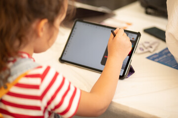 Little girl drawing on digital tablet using a digitized pen. Children's engagement of digital...