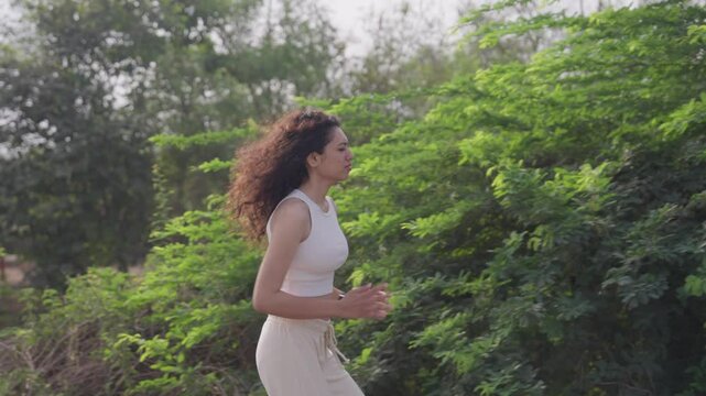 A side-view, slow-motion footage of a young south Asian fit woman jogging in the park in the early morning
