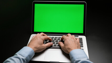 Hands typing on a laptop keyboard with a green screen in a dark setting