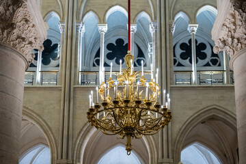 Golden chandelier hanging in the nave of Notre-Dame cathedral in Paris, with gothic arches in the background. Photographed in Notre Dame, Paris, French heritage, architecture detail