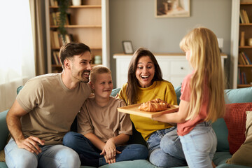 Happy  family enjoying in their time at home while daughter is bringing croissants to her parents...